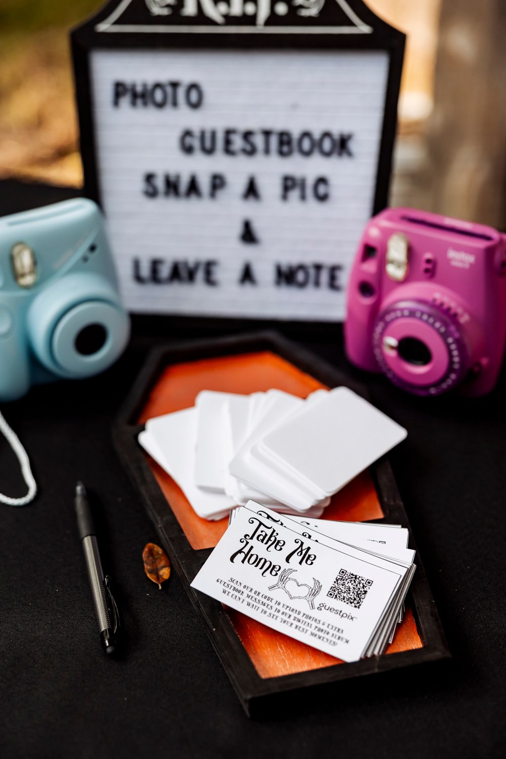 Wedding photo station setup with blue and pink Instax cameras and a guestbook sign.