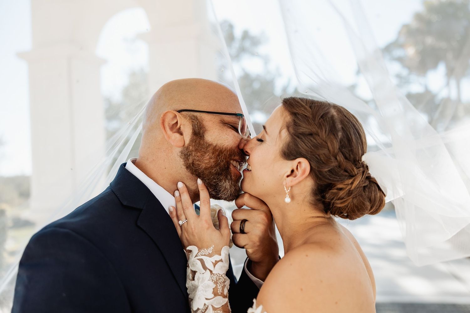 Bride and groom sharing a close intimate kiss under a flowing veil on their wedding day.