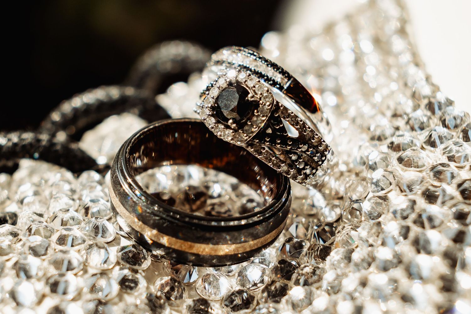 Black diamond engagement ring and matching wedding band displayed on a sparkling crystal surface.