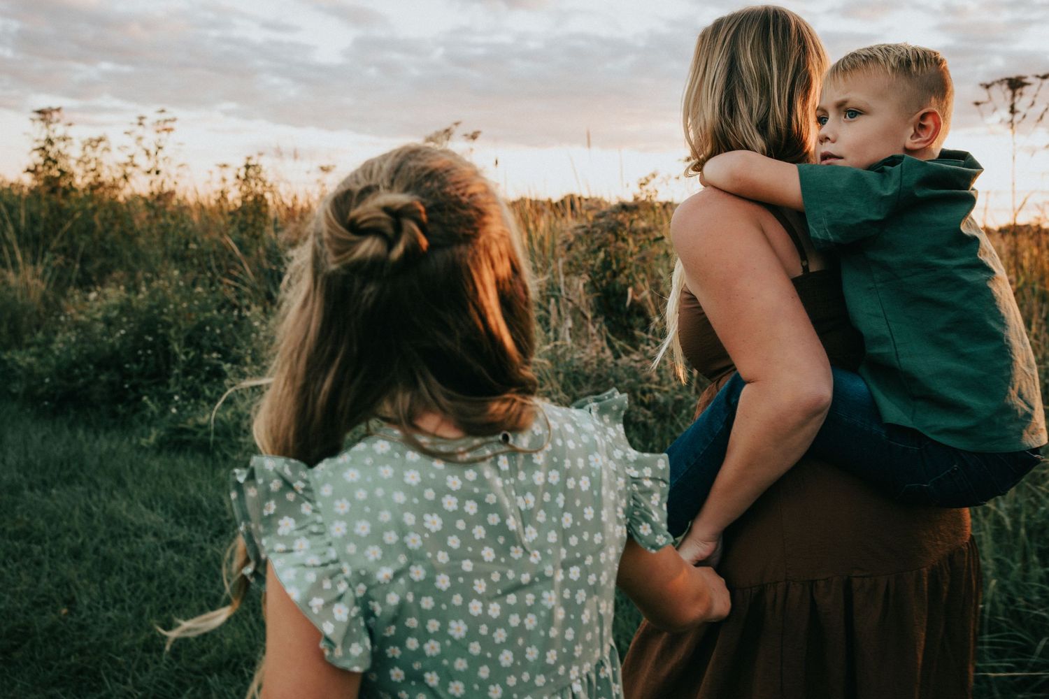 Three people enjoying a peaceful sunset moment together in a grassy field.
