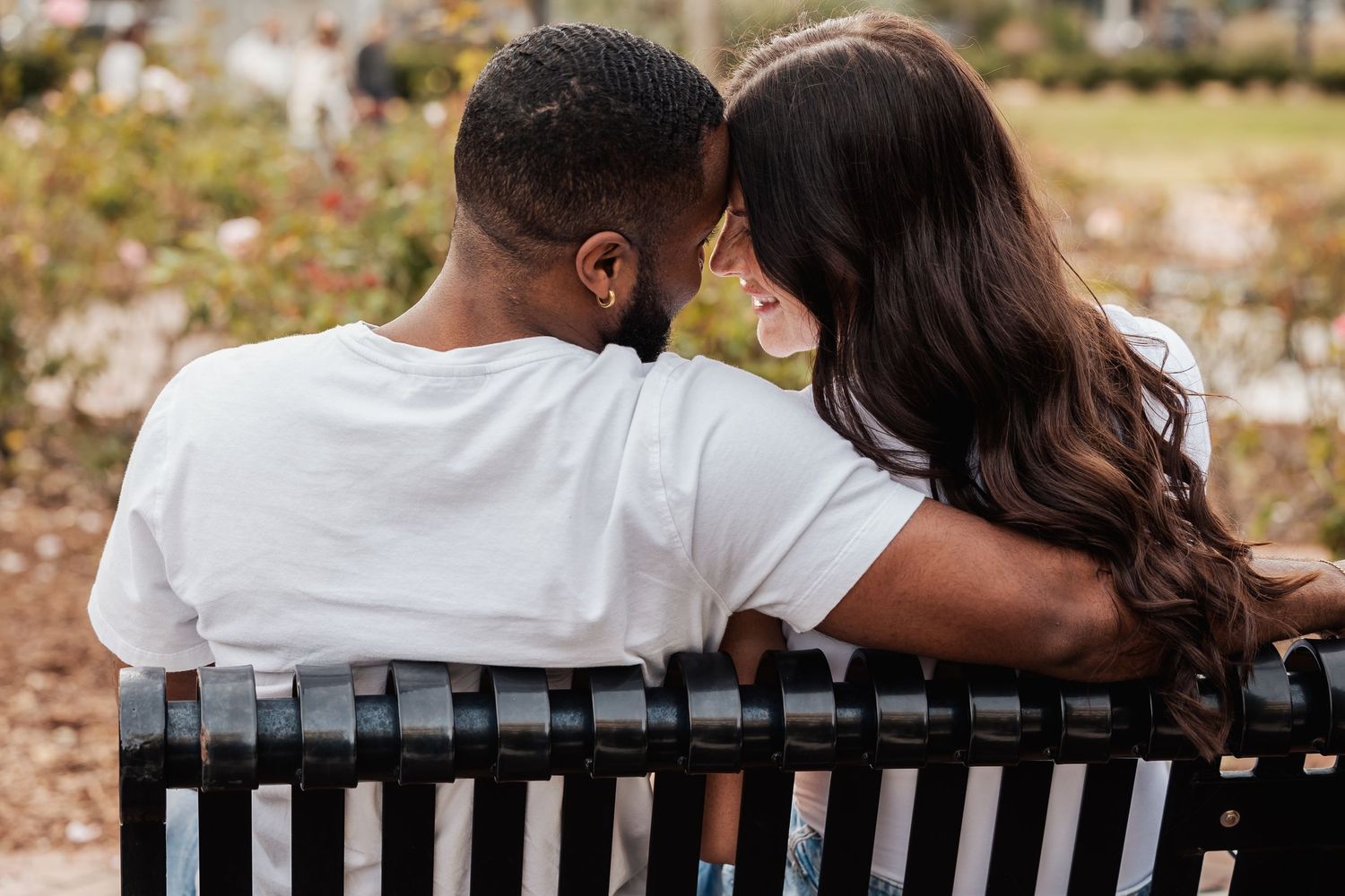 A couple sits close together on a park bench sharing an intimate moment.