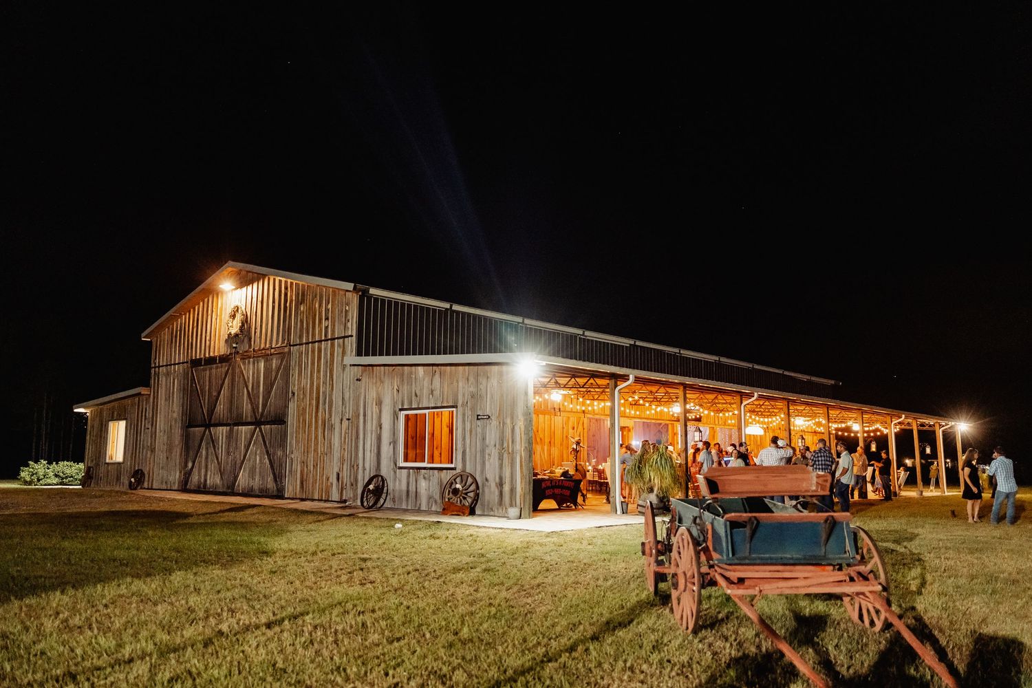 Rustic barn wedding venue illuminated at night with vintage wagon in foreground.