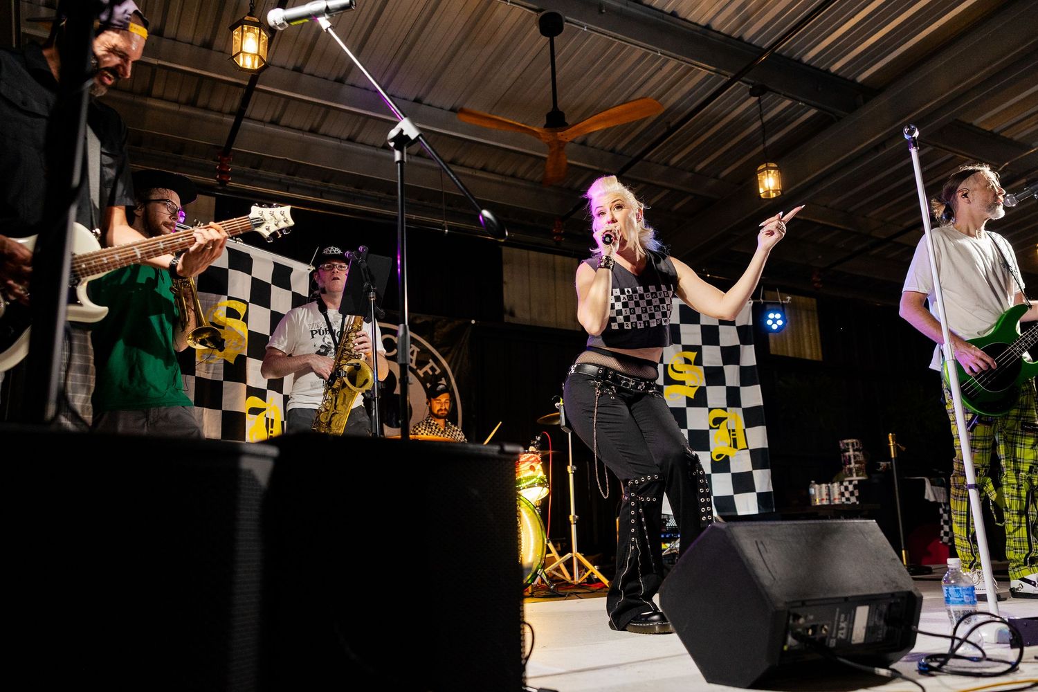Female singer performs with full band on outdoor stage with checkered backdrop.