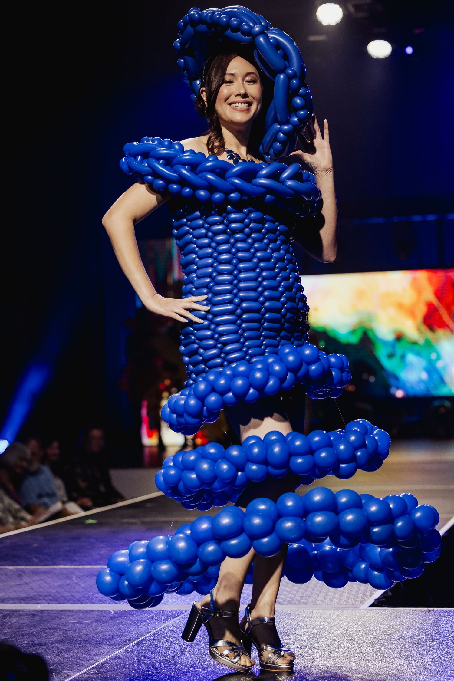 Model walks runway in an elaborate blue balloon dress with matching headpiece at a fashion show.