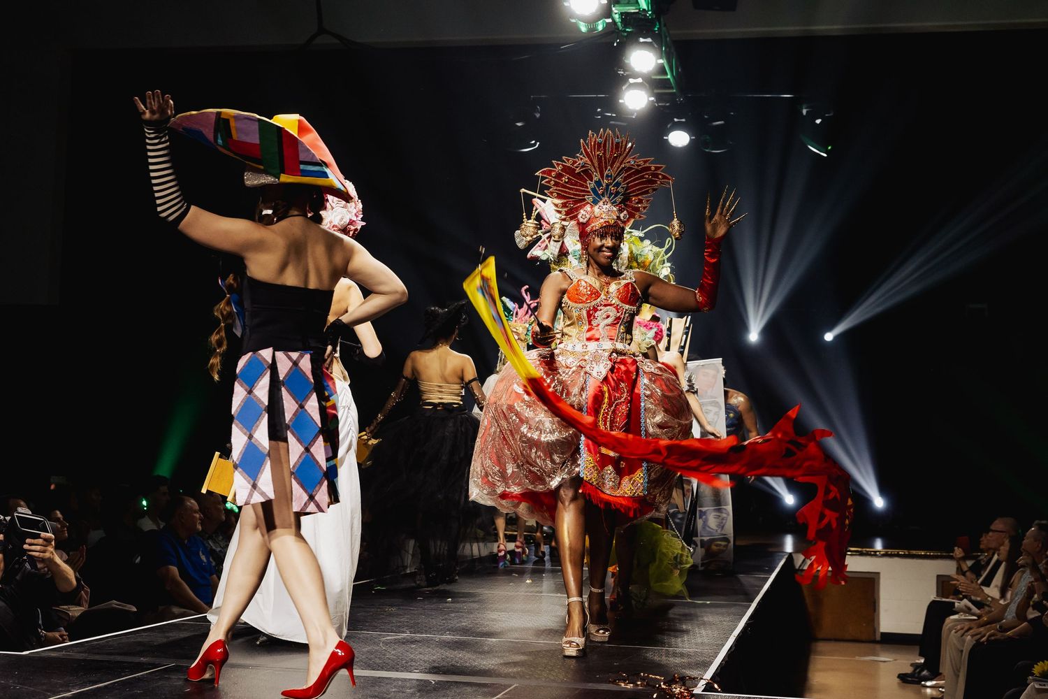 Models in elaborate carnival costumes walking on fashion show runway.