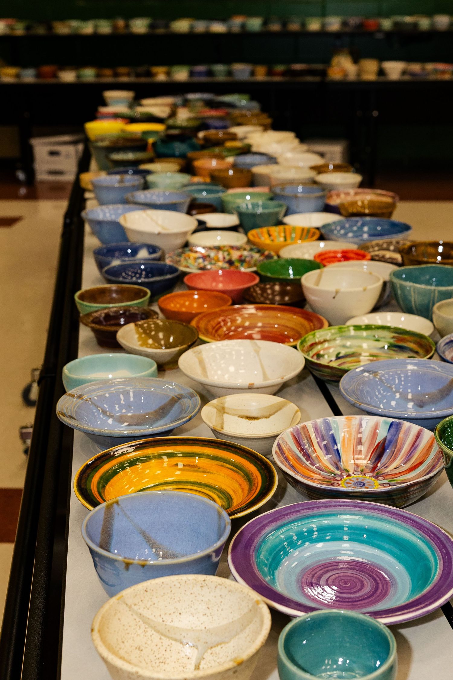 Rows of colorful handmade ceramic bowls displayed on long tables at a charity event.