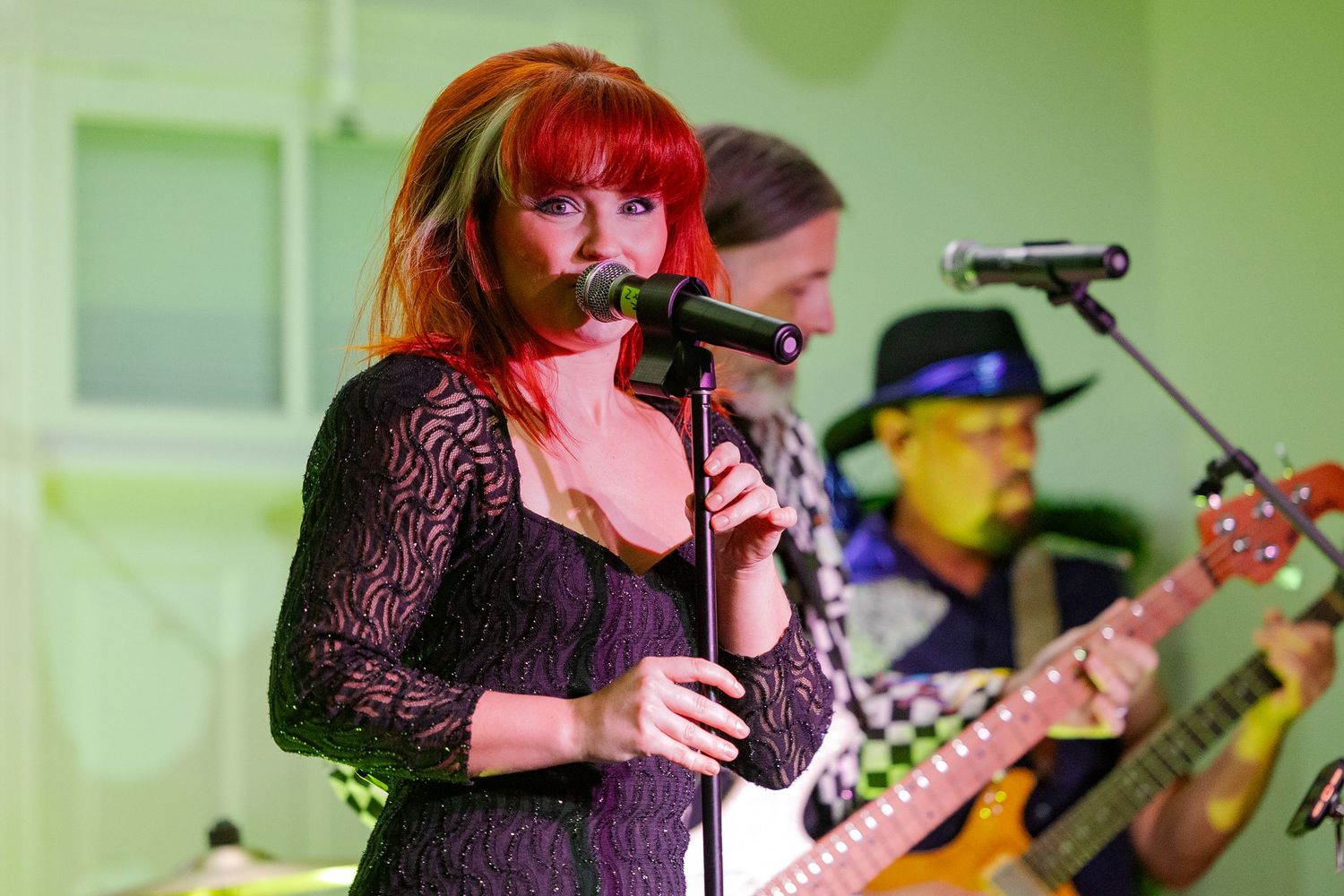 Red-haired female vocalist singing into microphone on stage with guitarist performing live band concert.