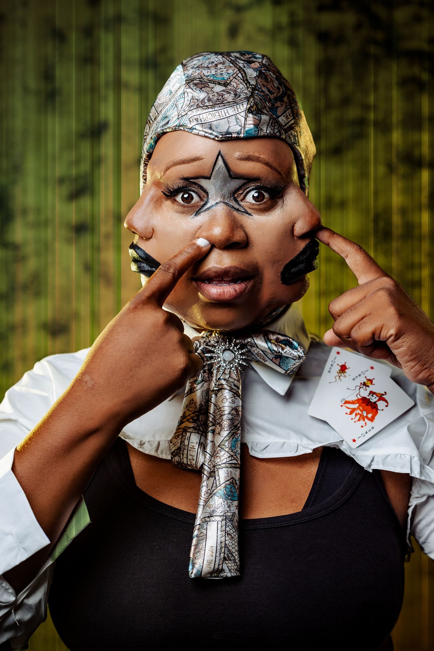 Expressive theatrical portrait with star makeup and metallic accessories against green background.