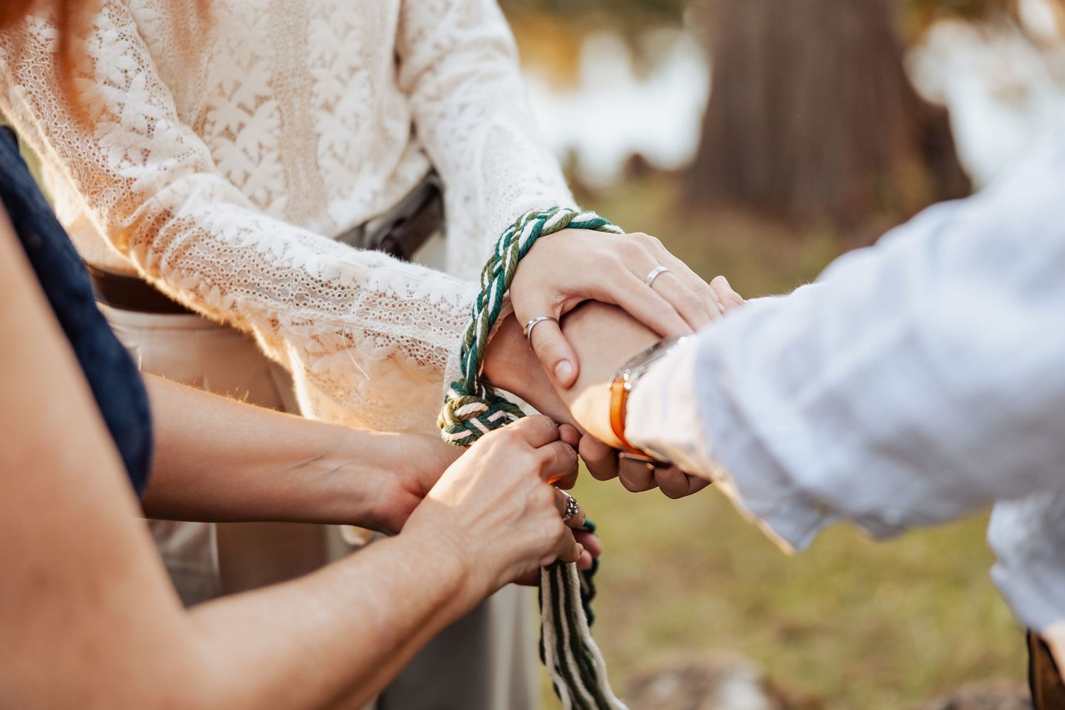 Close-up of hands being bound together with a braided cord during a handfasting wedding ceremony.
