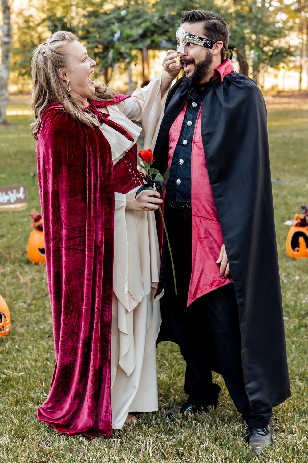 Couple in Halloween costumes, vampire and queen, share a playful moment outdoors at festive party.