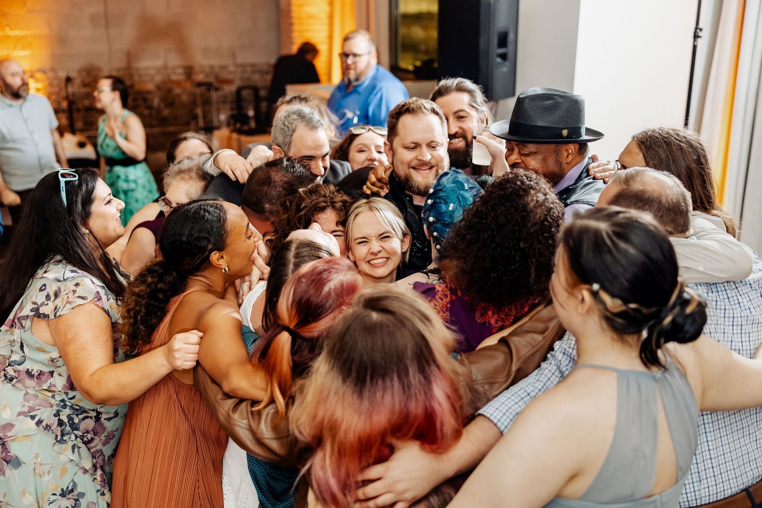 Joyful wedding guests sharing a group hug on the dance floor during a lively reception celebration.