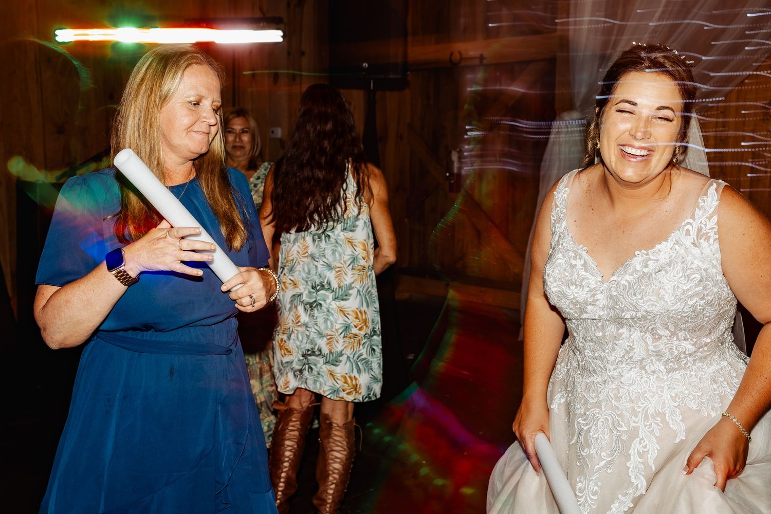 Wedding celebration with guests dancing and laughing in rustic barn setting.