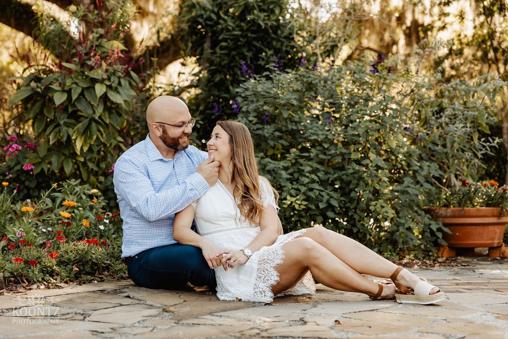 A romantic couple sitting together in a garden setting with lush greenery in the background.