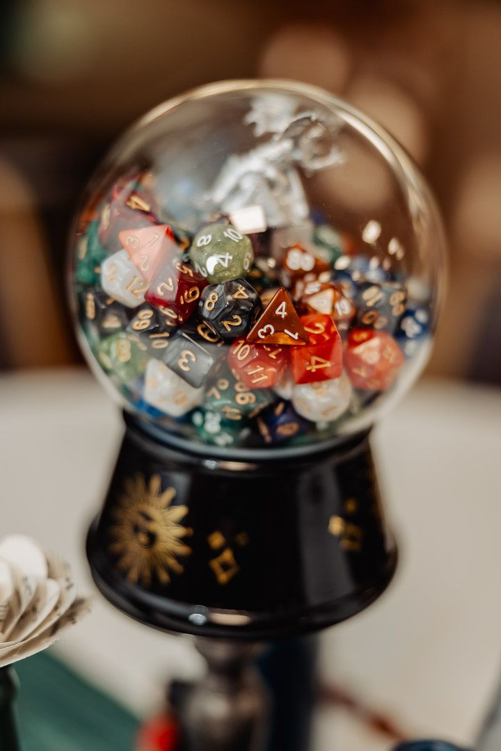 A glass globe filled with colorful gaming dice on a decorative black base with celestial designs.