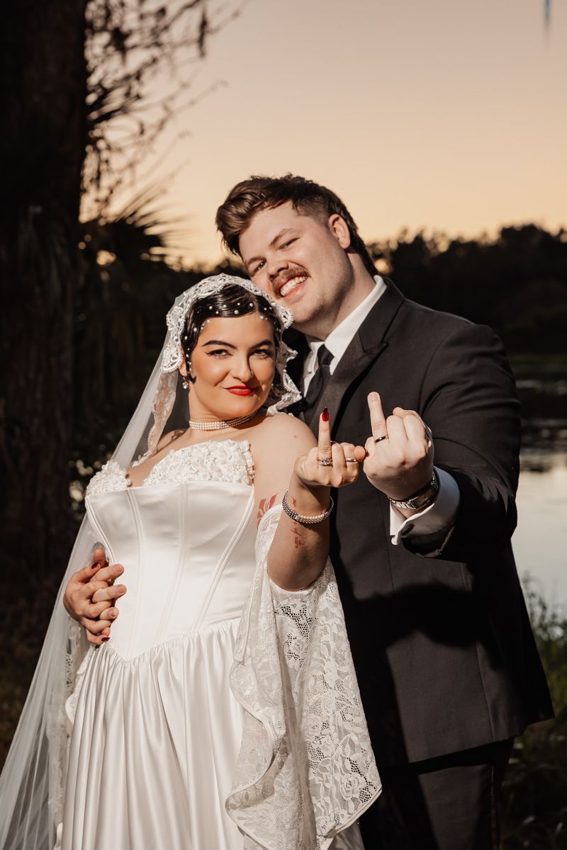 Smiling bride and groom showing off wedding rings at outdoor sunset wedding reception.