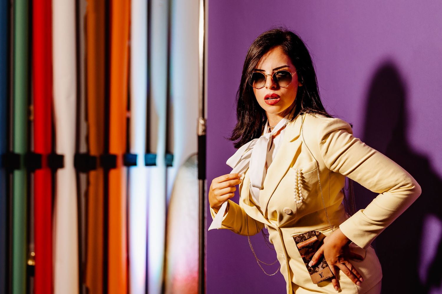 Stylish woman in cream blazer poses confidently beside colorful fabric rolls on purple background.