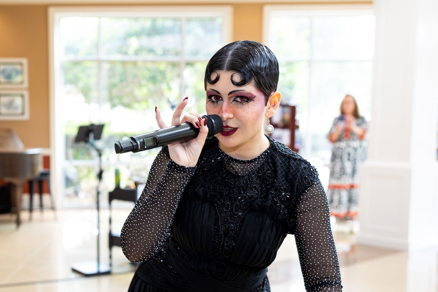 Singer in black beaded gown performs with microphone at formal event.