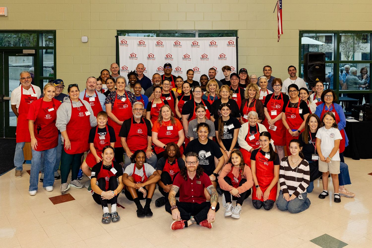 Large group of community volunteers in red and black aprons posing together indoors.