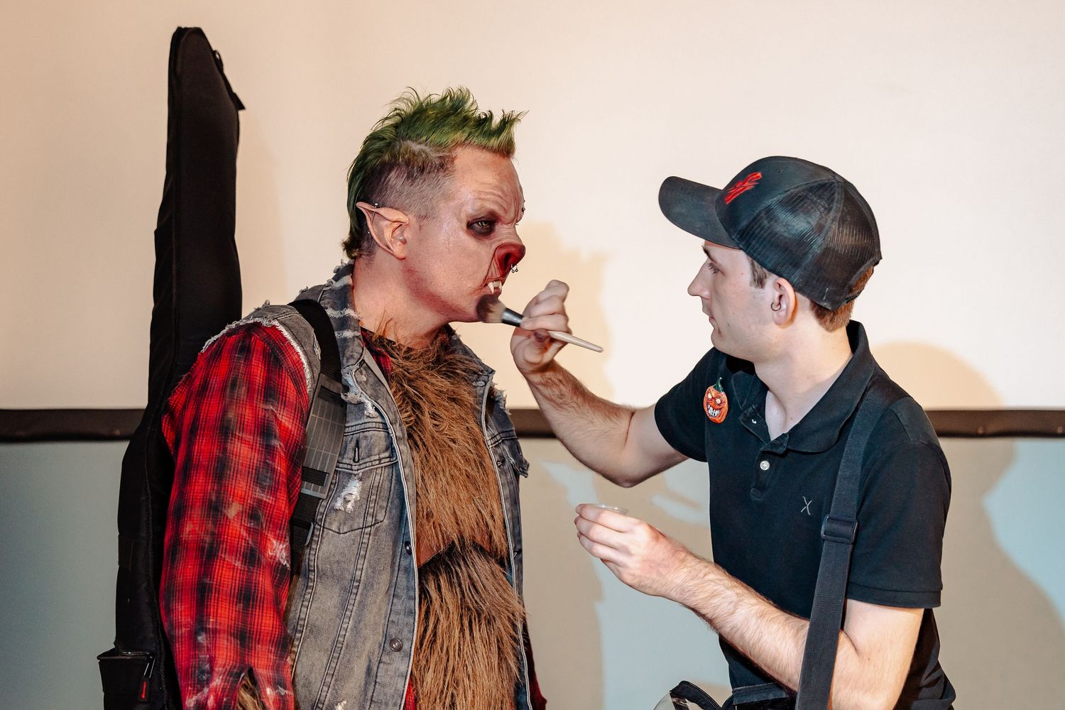 Behind the scenes makeup application with artist working on performer in plaid shirt.