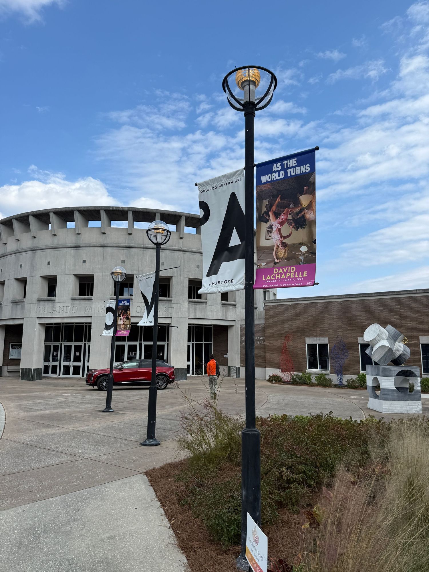 A series of connected brick buildings with a lamp post and signage under a bright blue sky with white clouds.