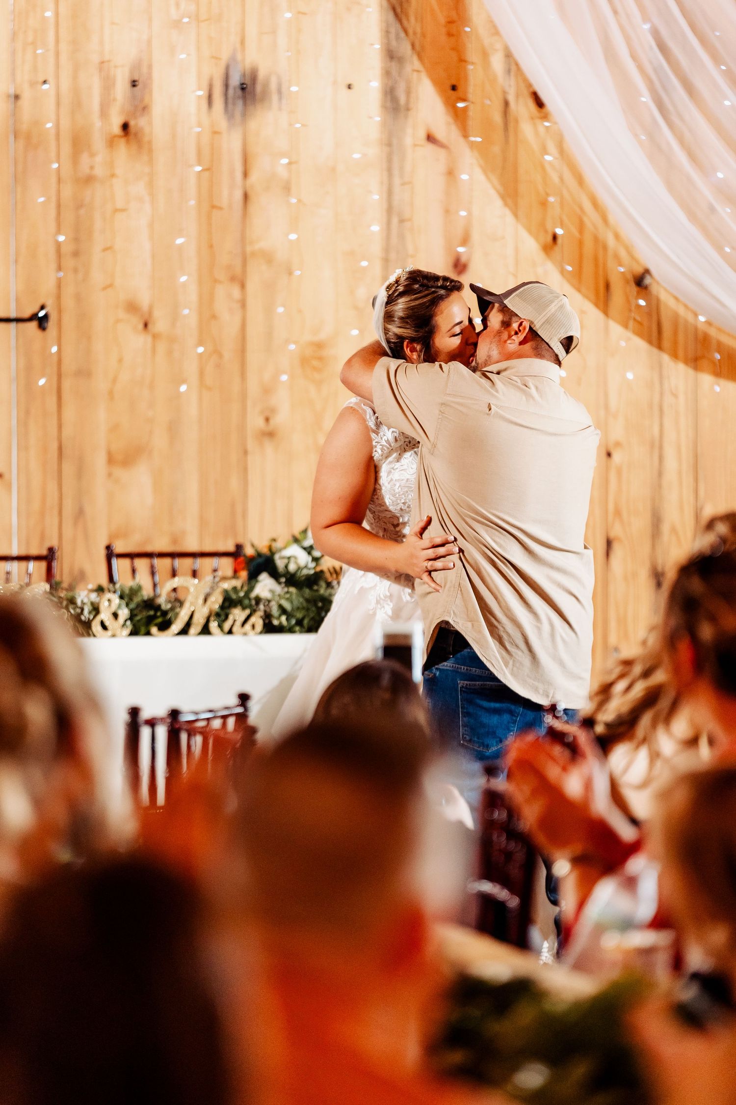 Wedding couple shares passionate dance surrounded by guests in rustic wooden barn setting.