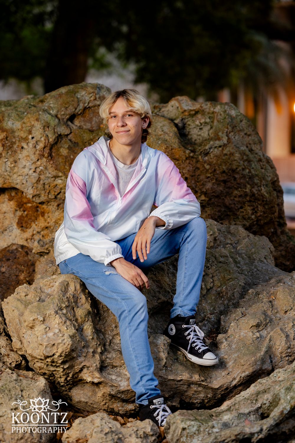 Casual portrait seated on large rock formation wearing pink and white jacket.