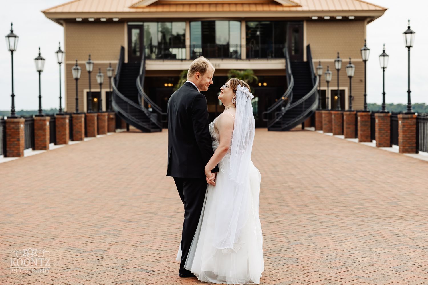 Wedding couple in front of Mediterranean venue with brick patio and decorative lamp posts.
