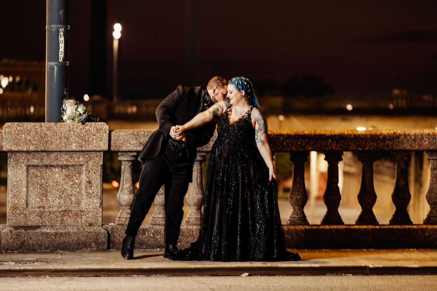 Gothic wedding couple sharing tender moment by stone balustrade at night outdoor venue.