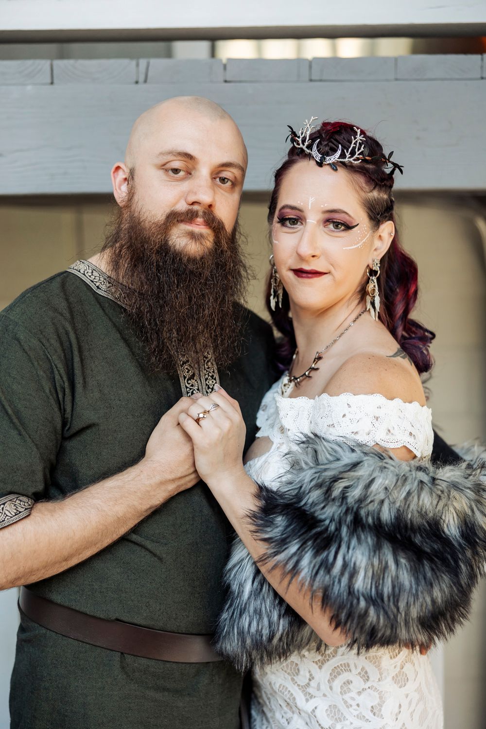 Viking-themed wedding couple poses together, bride in antler crown and fur stole, groom in green embroidered tunic.