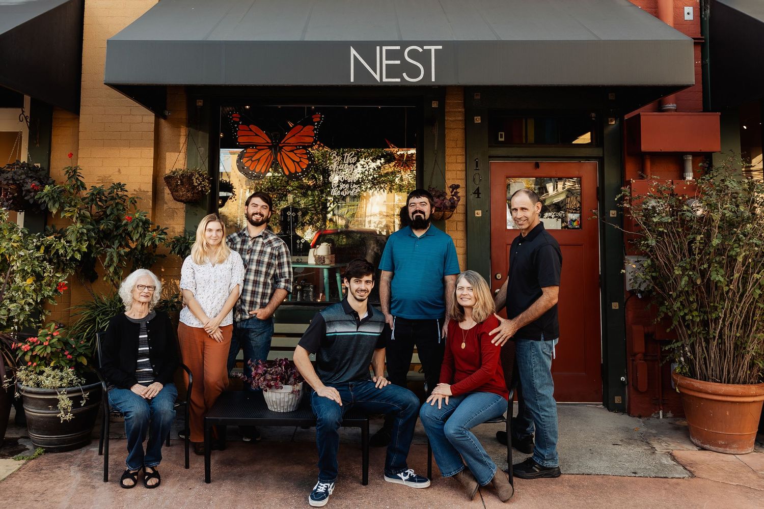 Extended family group portrait posed outside a shop called Nest with butterfly decor.