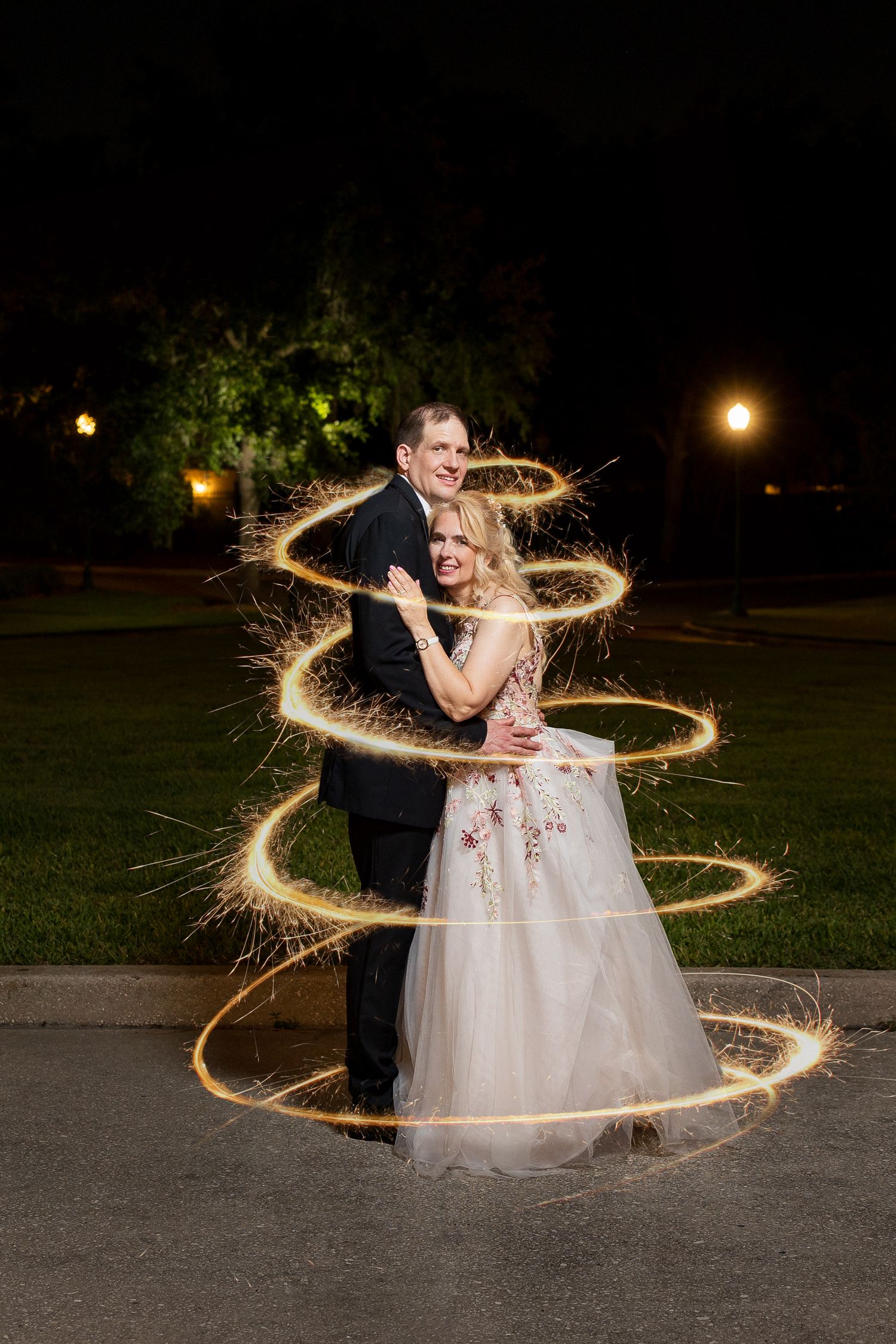 Bride and groom embrace surrounded by swirling sparkler light trails in a stunning nighttime photo.