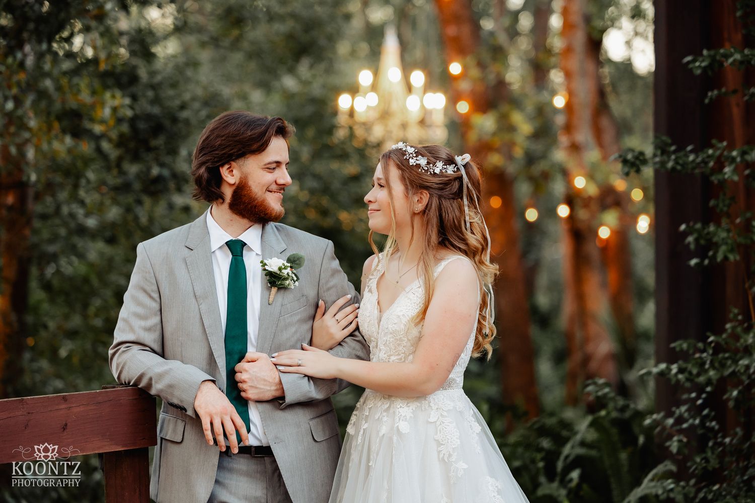 Bride and groom share a joyful glance under a chandelier at their rustic outdoor wedding venue.