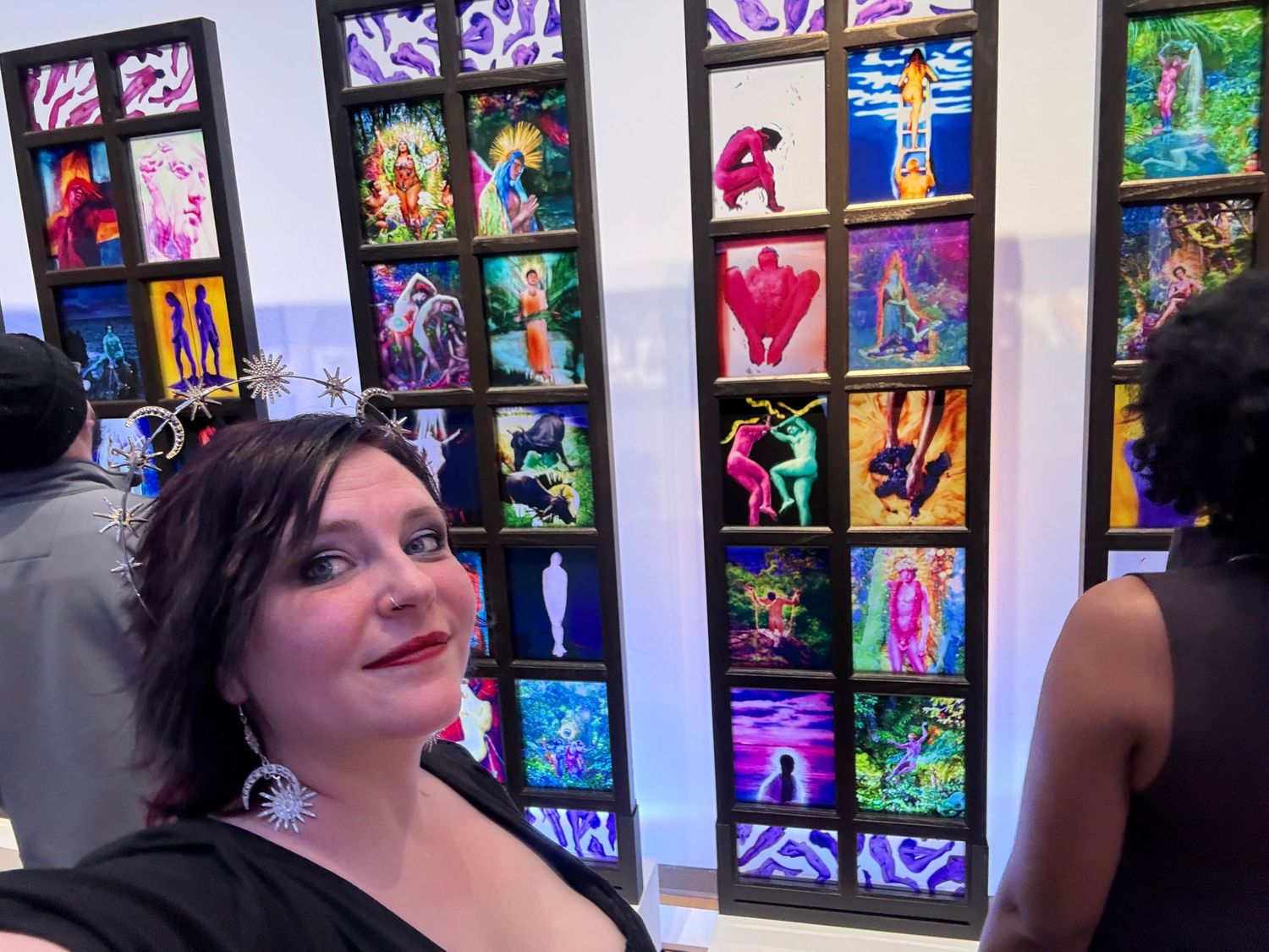 A wall display of colorful illuminated art pieces and photographs arranged in a grid pattern at a gallery.