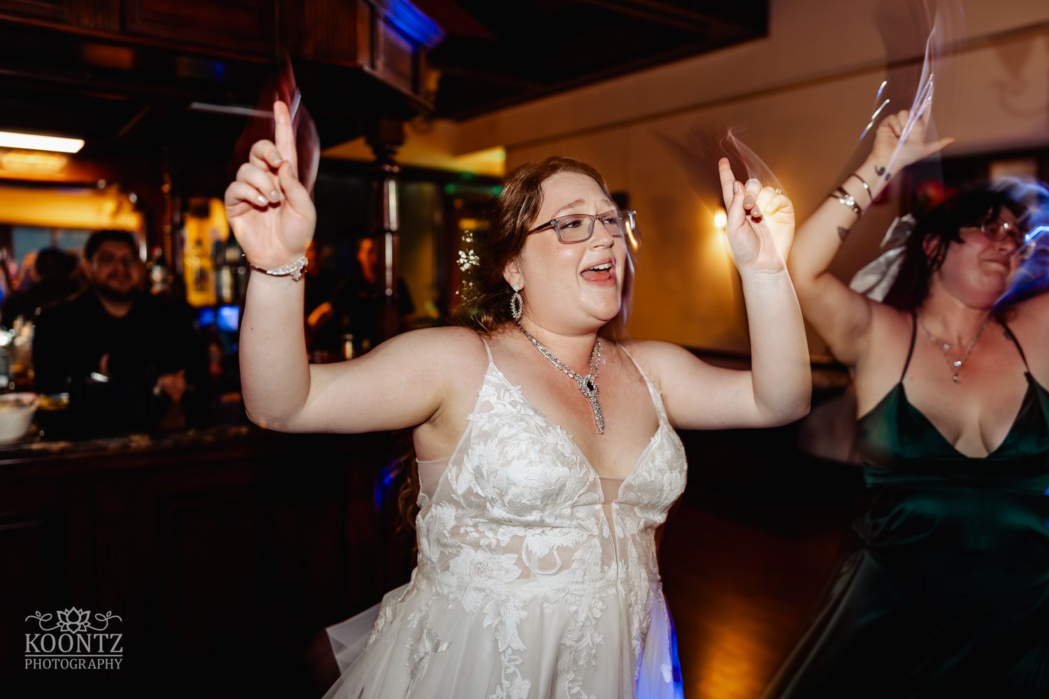 A bride dances joyfully with raised arms during wedding reception celebrations.
