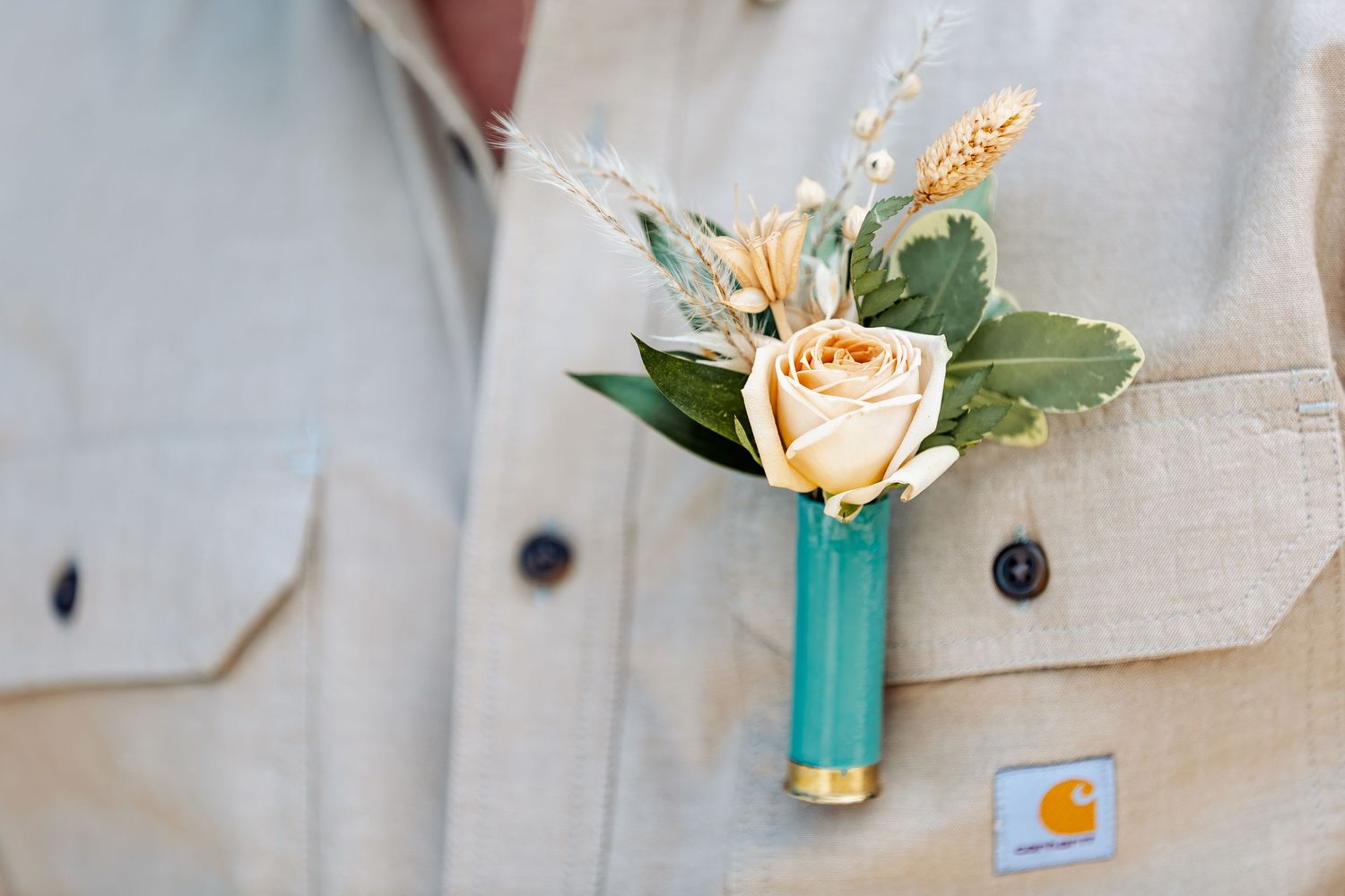Delicate boutonniere with peach rose and wheat accent pinned to light colored shirt.