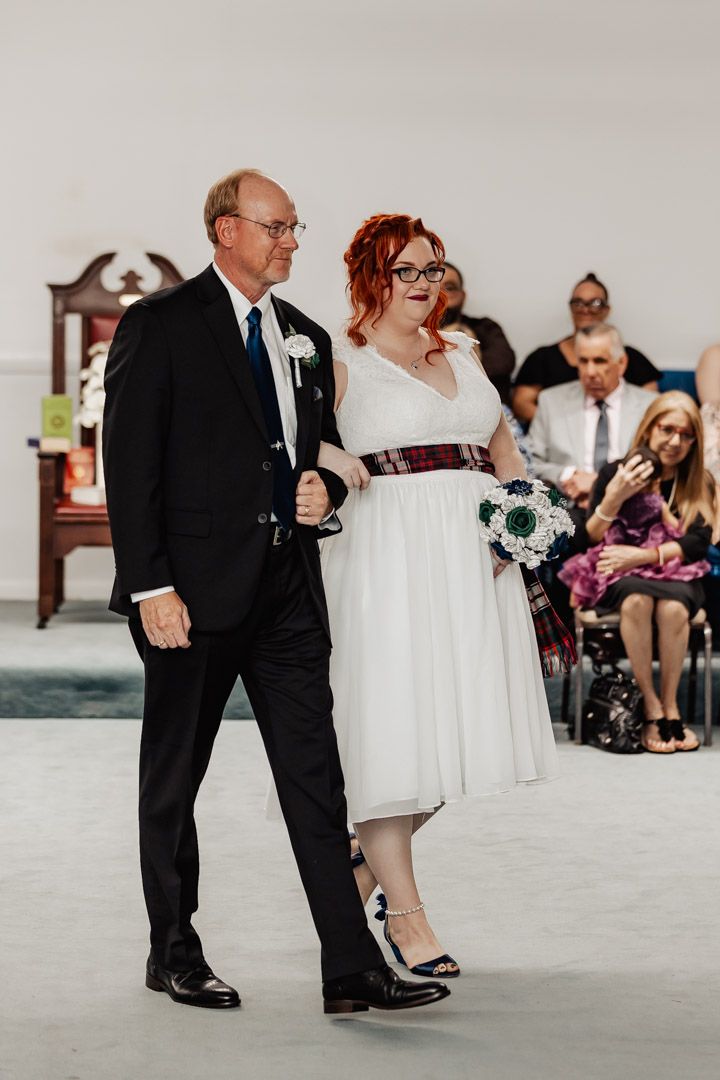 A wedding processional showing a couple walking down the aisle in a ceremony space with guests seated.