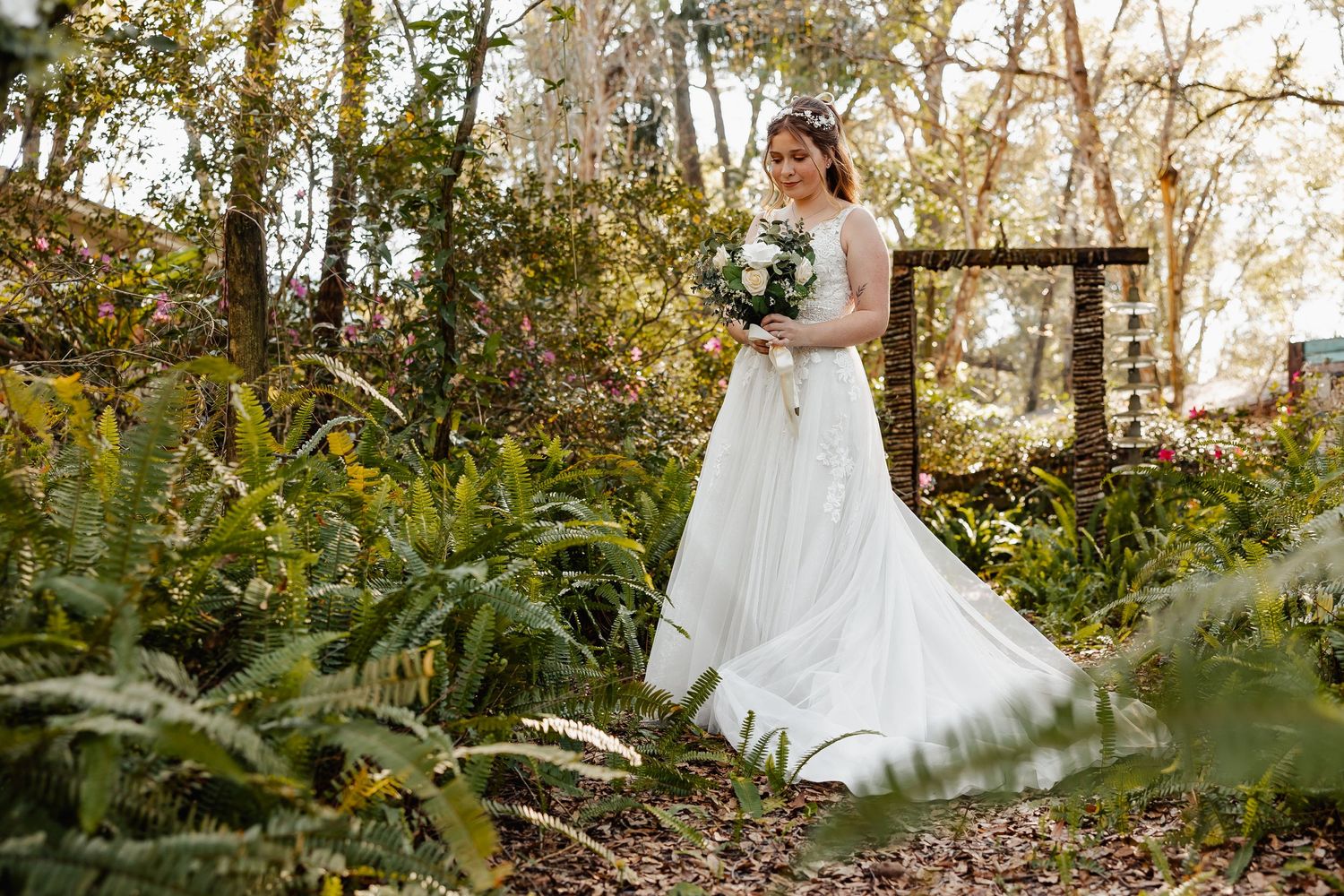 An elegant bridal portrait showcasing a white wedding gown among garden ferns and greenery.