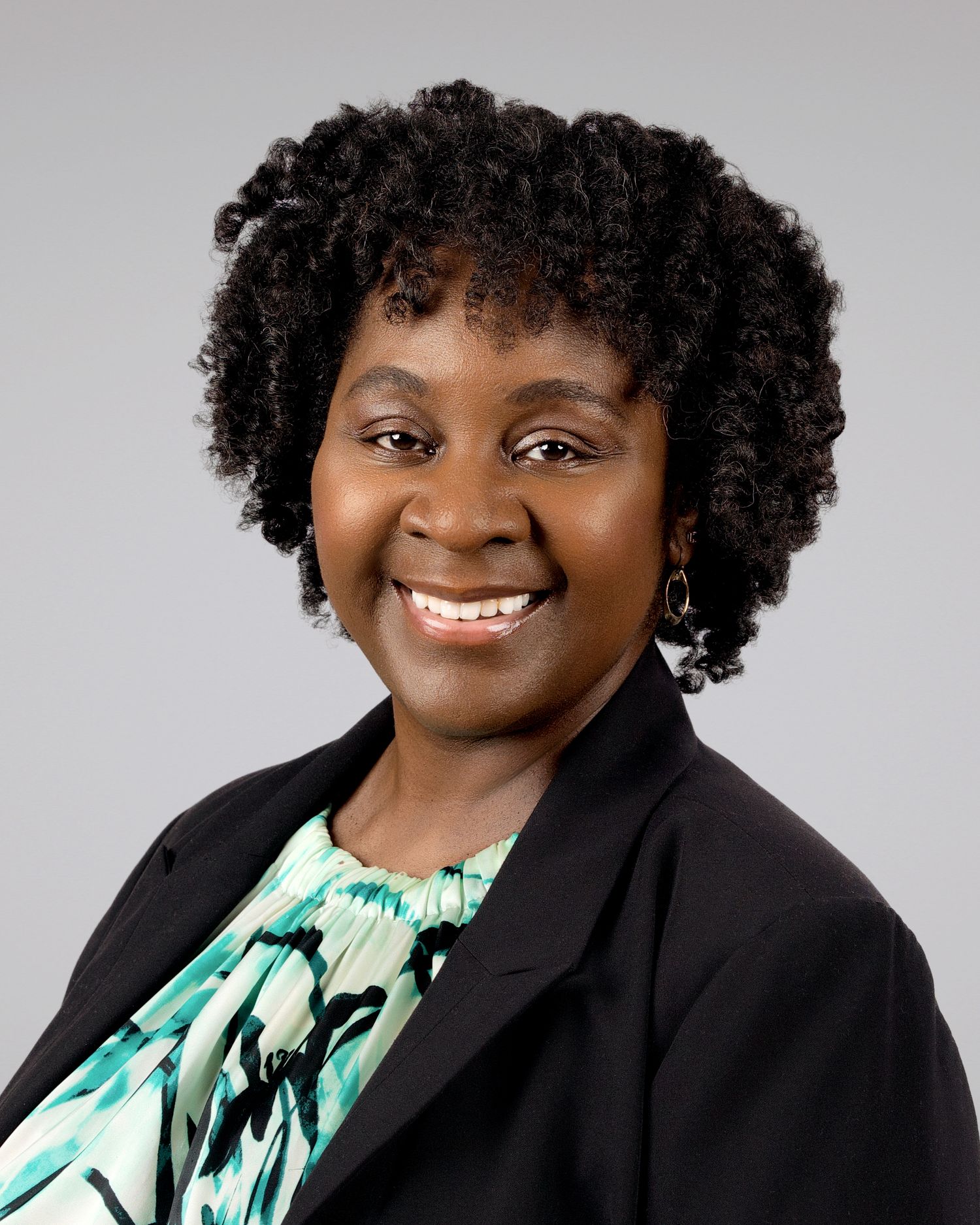 Smiling Black woman with natural curly hair wearing a black blazer and floral top.