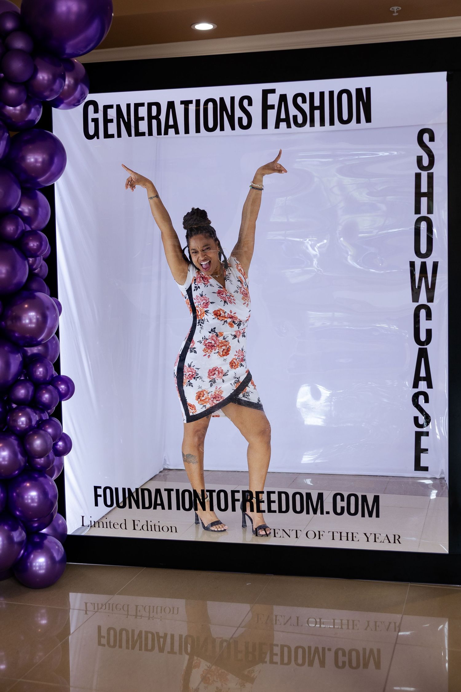 Excited woman poses at the Generations Fashion Showcase banner by Foundation to Freedom event display.