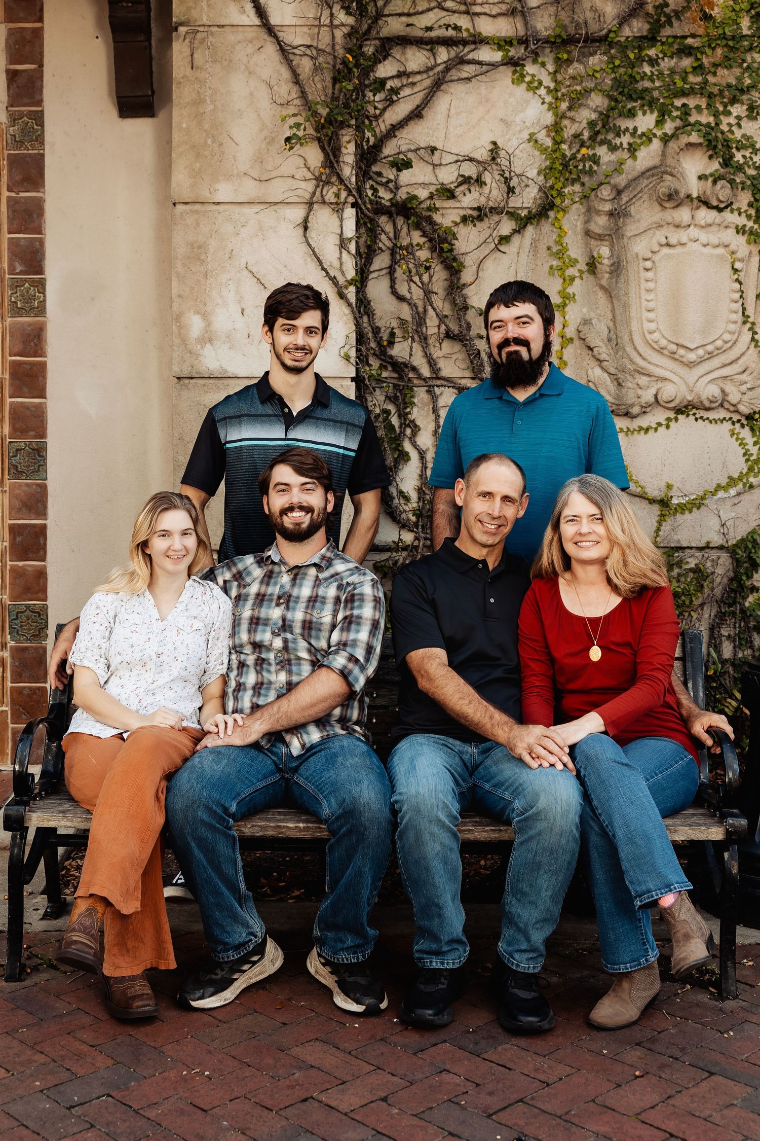 Extended family of six posing on a bench surrounded by ivy-covered stone wall.