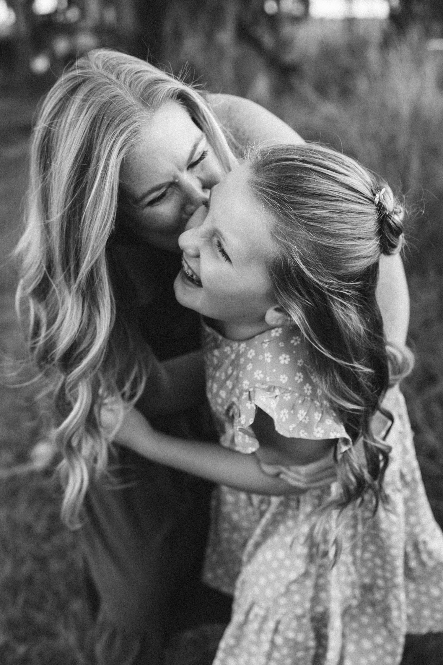 Black and white photo of mother and daughter sharing a tender nose-to-nose moment outdoors.