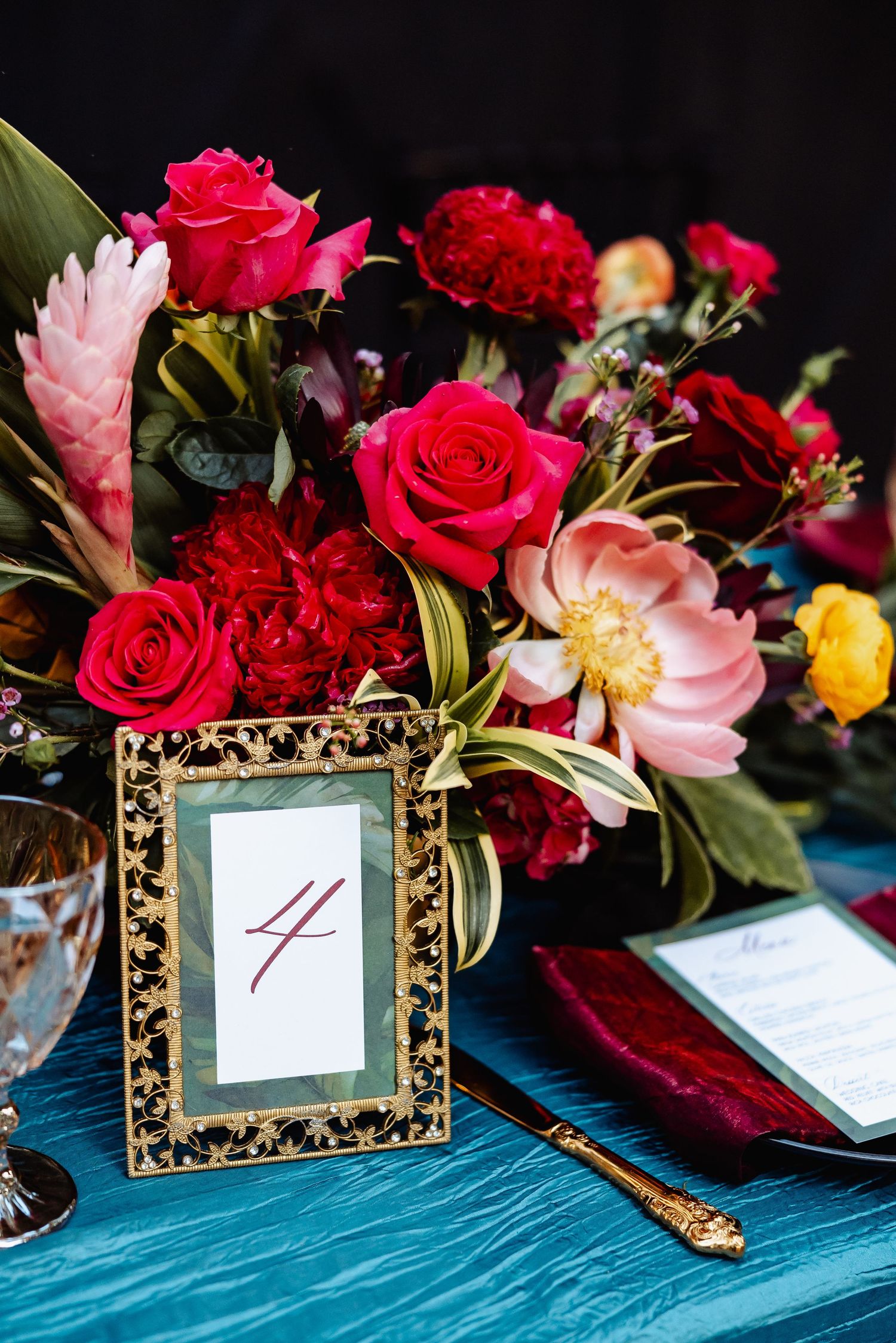 Elegant wedding table centerpiece with red roses and gold table number four.