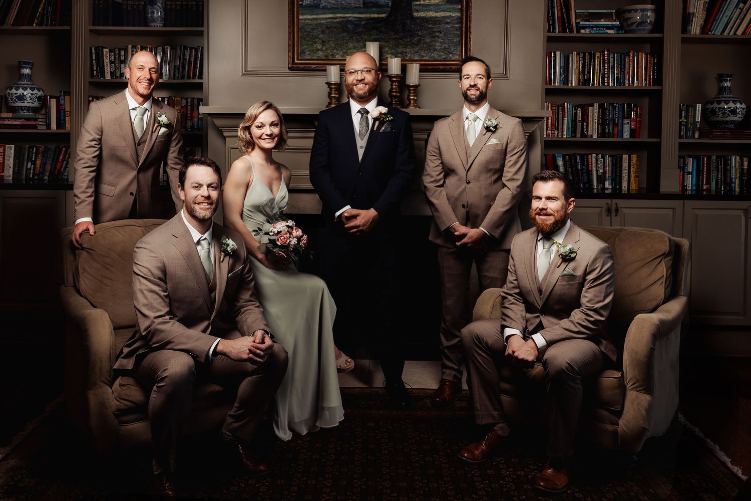 Groomsmen and bridesmaid in tan suits and sage dress posing in a library setting.