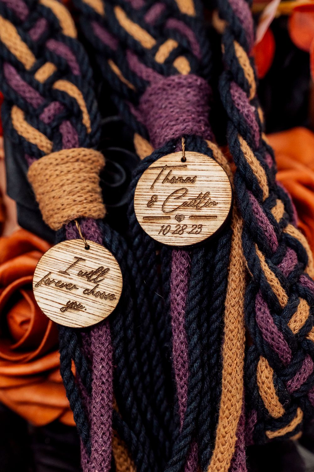 Braided handfasting cord in navy, purple, and gold with engraved wooden tags reading Thomas and Caitlin 10-28-23.