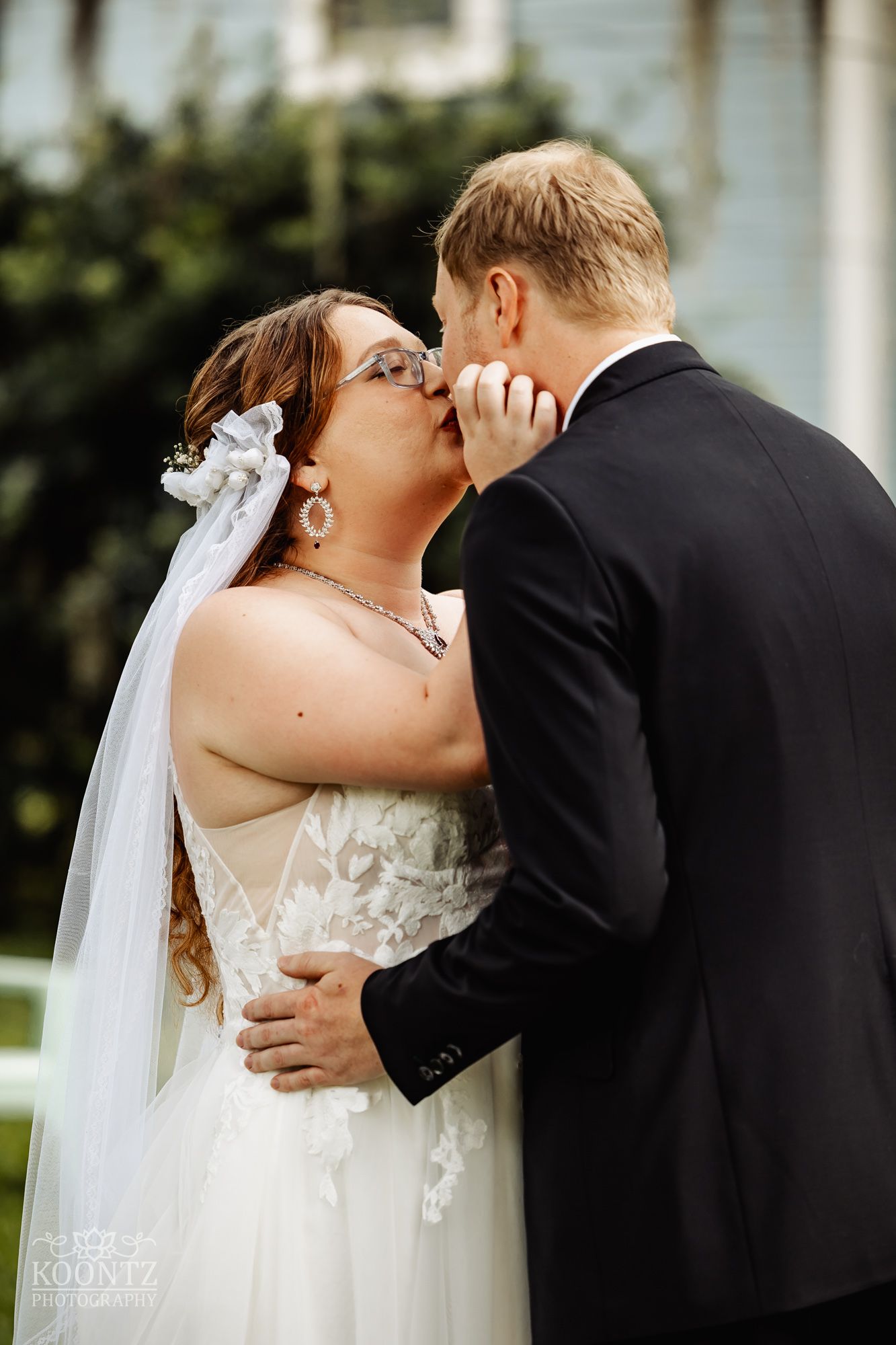A romantic wedding day kiss between newlyweds in a garden setting with Spanish moss in background.