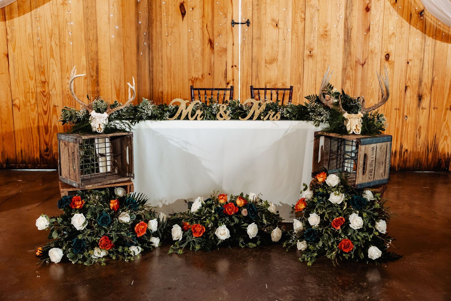 Wedding reception head table decorated with white linens and cascading floral arrangements.