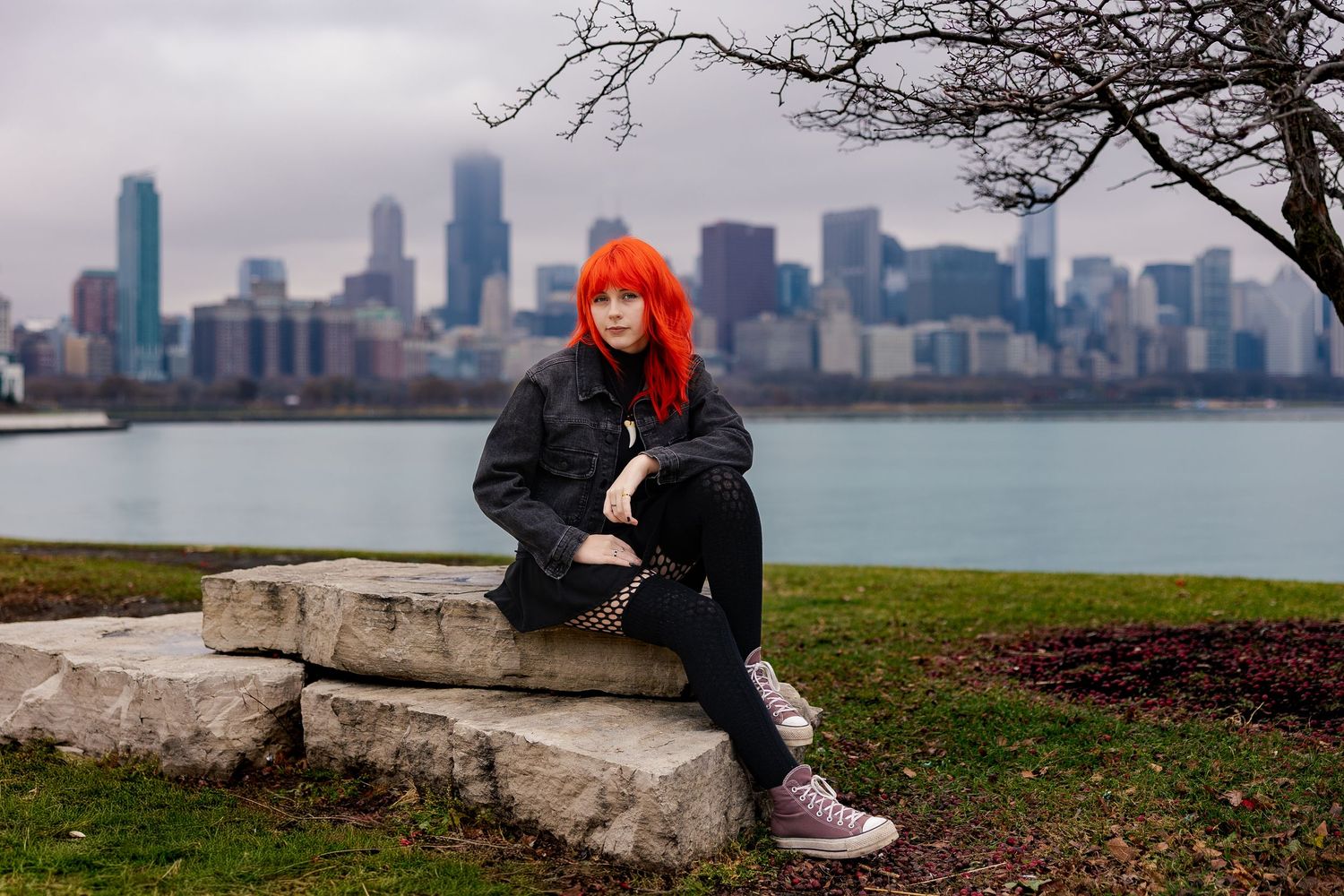 Woman with bright red hair sitting on stone steps with Chicago skyline and lake in background.