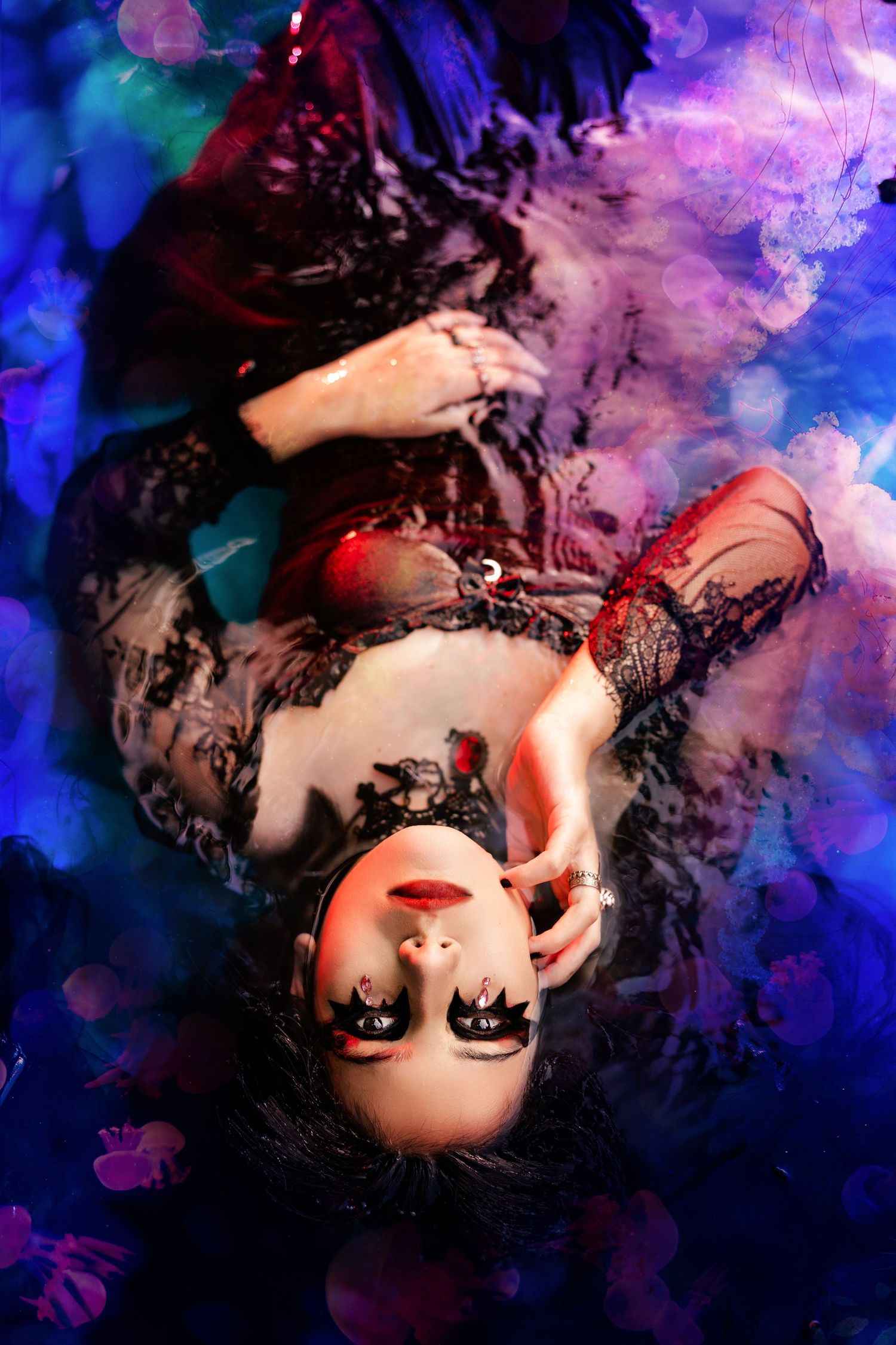 Woman with dramatic gothic makeup lies in water with purple smoke in dark fantasy portrait.