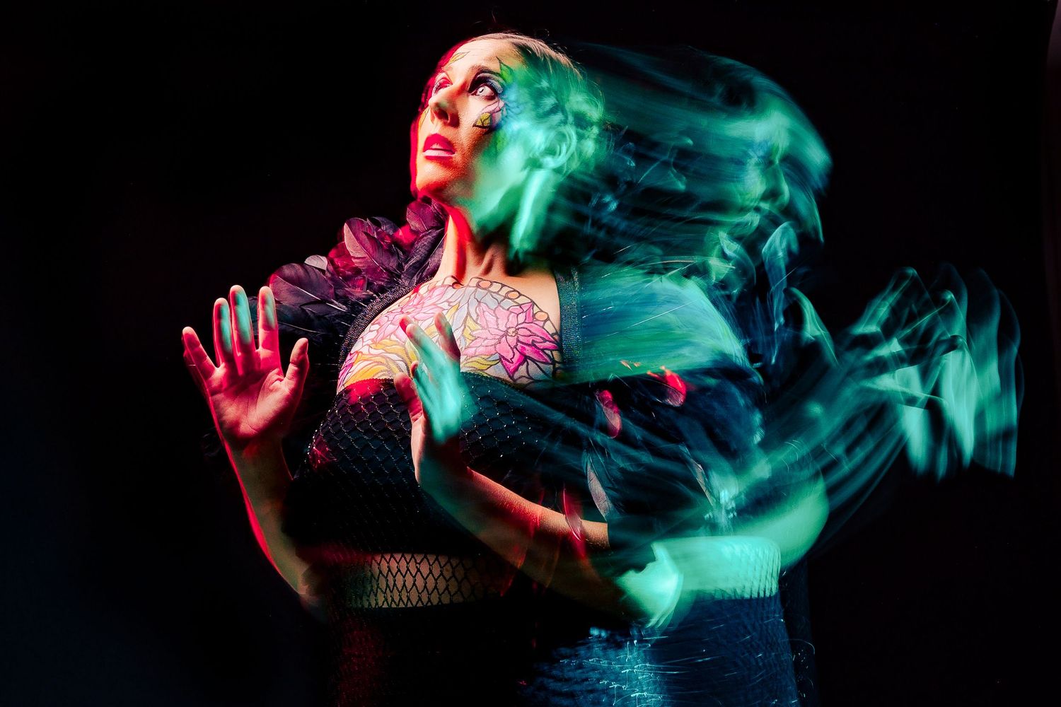 Woman with tattoos in dramatic long-exposure photo with green and red light trails on dark background.