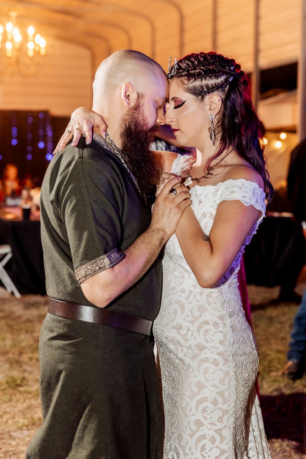 Bride and groom sharing intimate forehead touch during first dance at rustic indoor wedding reception with warm lighting.